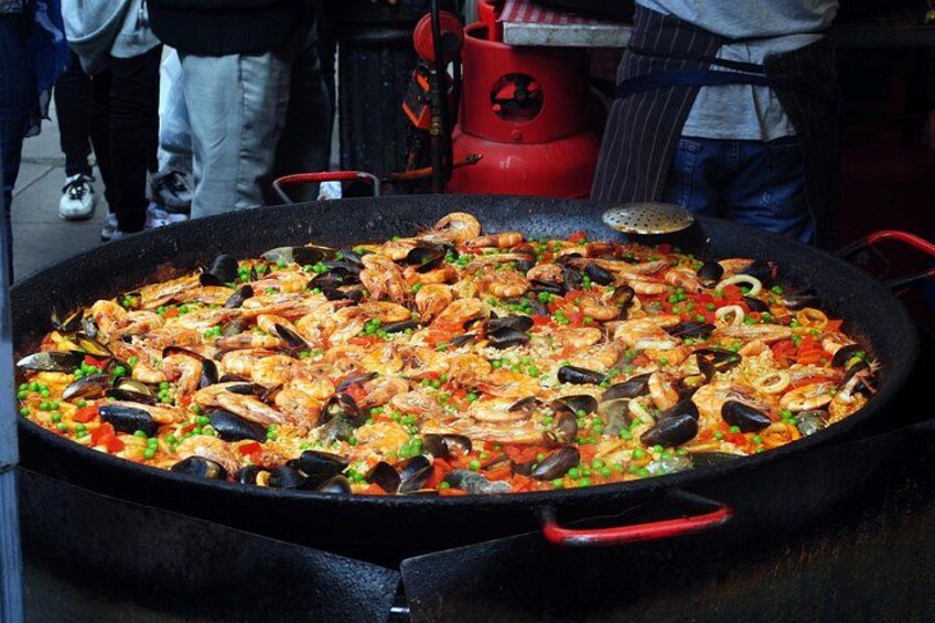 Een grote paella met zeevruchten in een zwarte pan met rode handgrepen. 1