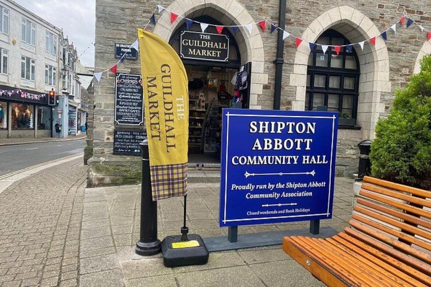A street with a building labeled 'The Guildhall Market' and a sign for 'Shipton Abbott Community Hall.' 2