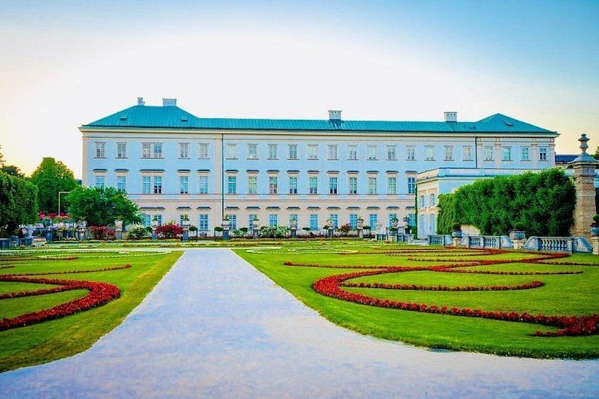 Ein großes, klassizistisches Gebäude mit einer symmetrischen Fassade, einem zentralen Weg und formal gestalteten Gartenanlagen. 5