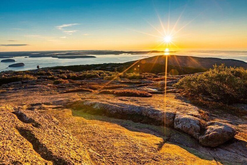 A sunset over a rocky landscape with a person standing on a hill. 1