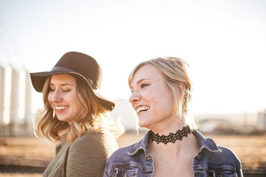 Two people outdoors, one wearing a hat and the other a denim jacket, with a blurred background suggesting an open area. 2