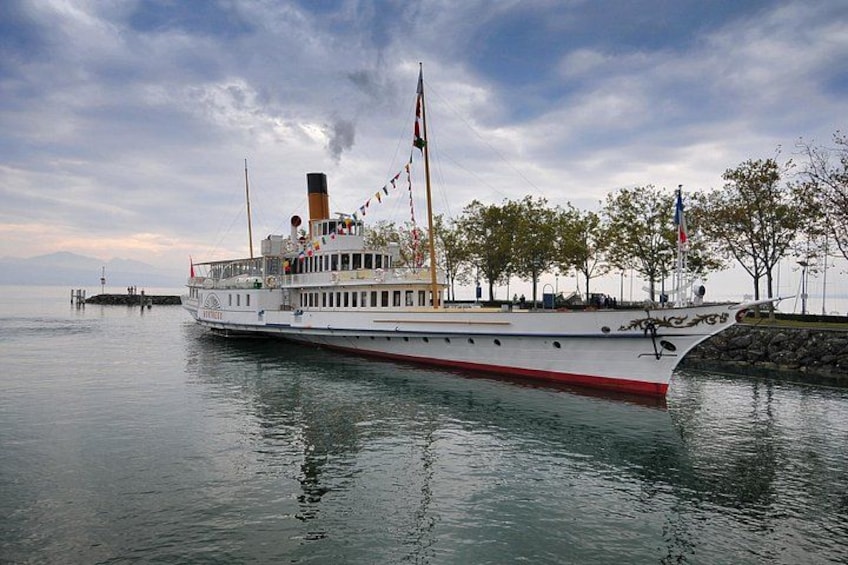 A large white boat with red trim docked at a pier, surrounded by trees and a cloudy sky. 1