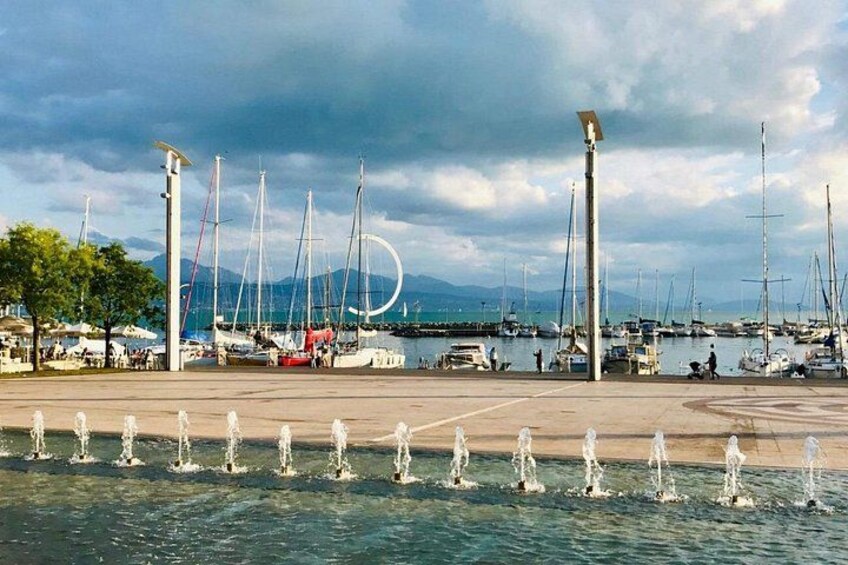 A marina with multiple sailboats docked, a fountain in the foreground, and a cloudy sky. 5