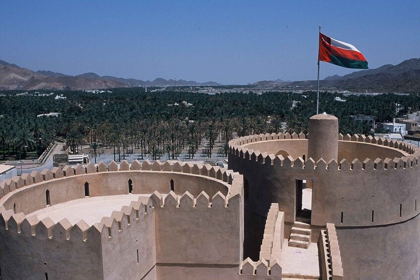 A historic fort with a flagpole, surrounded by palm trees and mountains in the background. 2