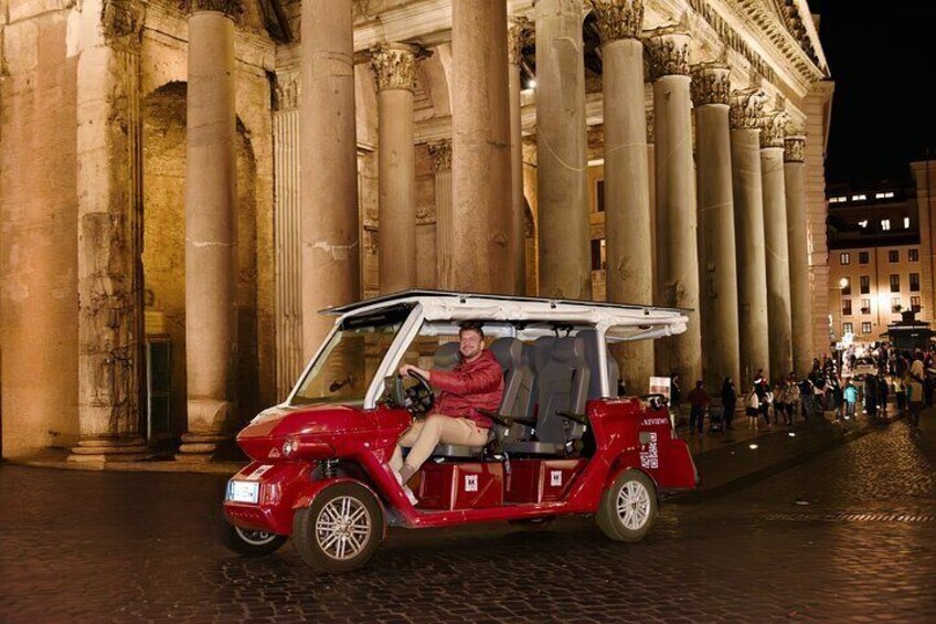 A red car with a roof rack parked in front of a historic building with large columns. 1
