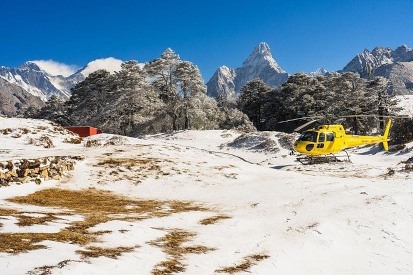 A yellow helicopter parked on a snowy mountain with a red building in the background. 2