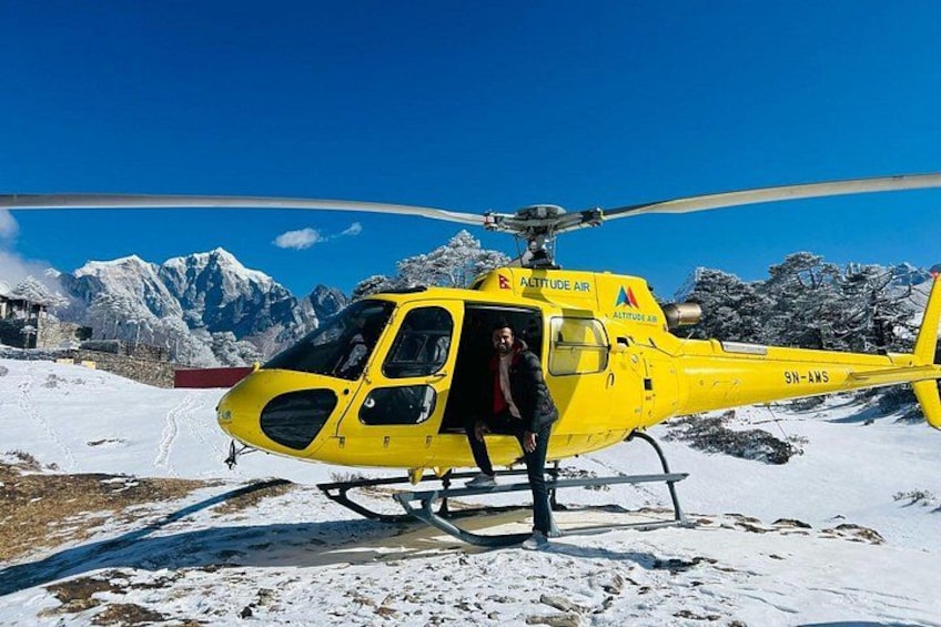 A yellow helicopter with 'Altitude Air' on the side parked on a snowy mountain with a clear blue sky. 5