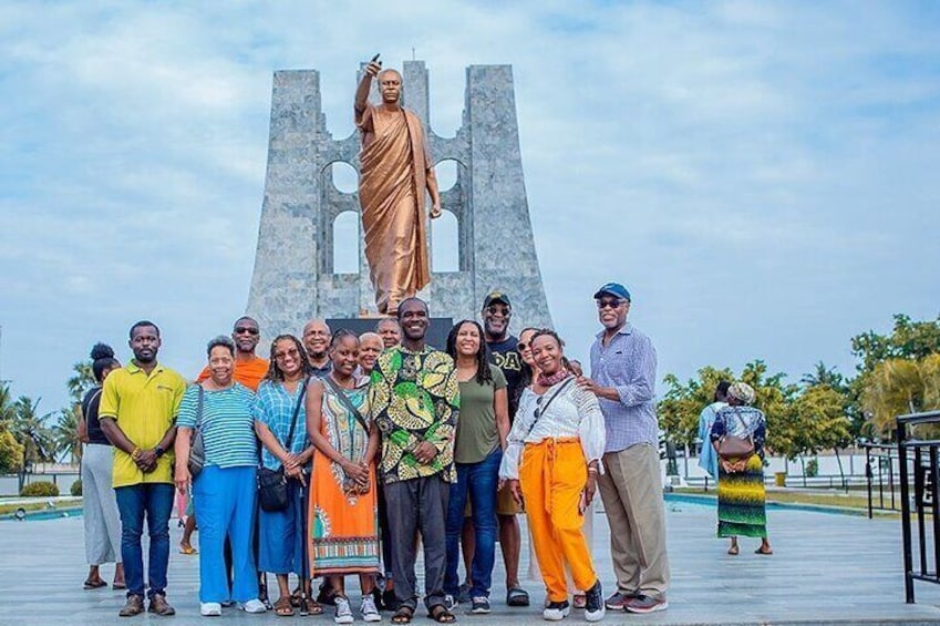Un grupo de personas de pie frente a una estatua, con una estructura grande al fondo. 1