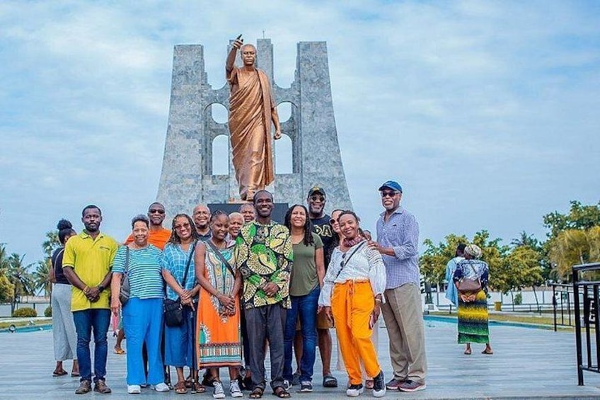 Un grupo de personas posando frente a una estatua, con un gran monumento al fondo. 1