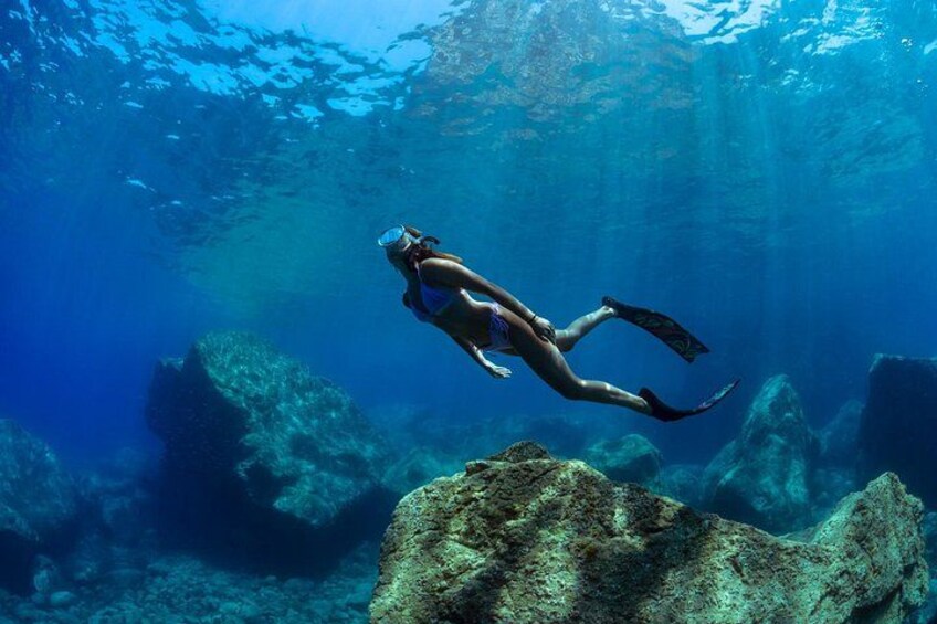 A person scuba diving underwater with rocks and marine life visible. 4