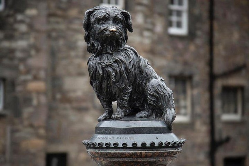 Een bronzen beeld van een hond op een voetstuk voor een stenen gebouw. 3