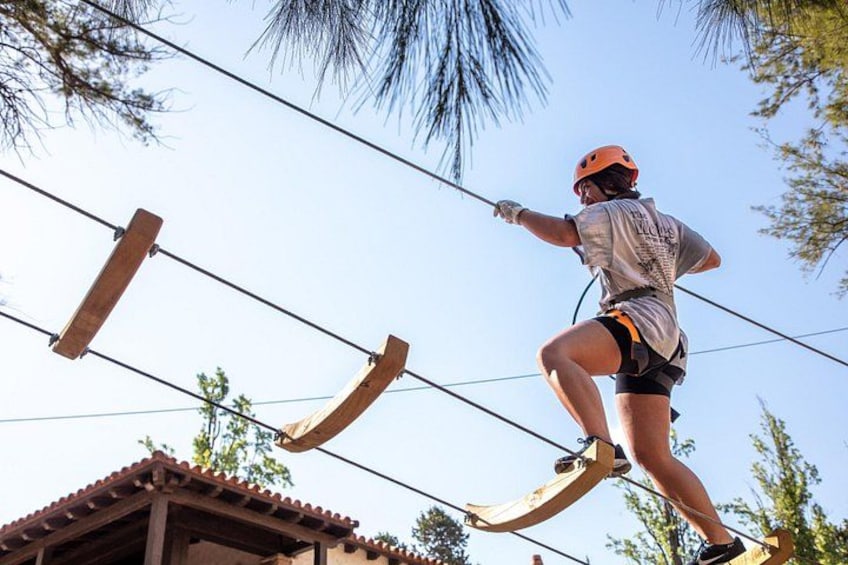 A person zip-lining, wearing a helmet and harness, between wooden structures. 4