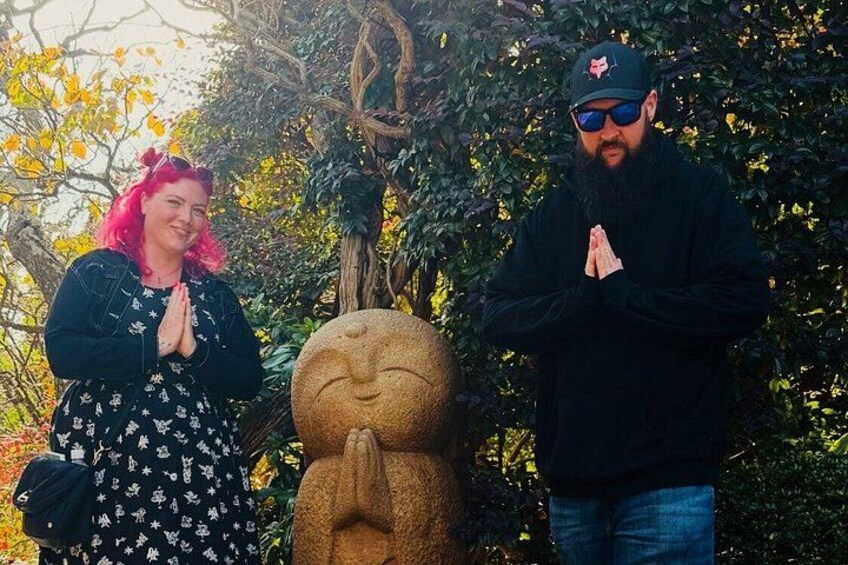 Two people standing in front of a stone statue with a praying gesture. 5