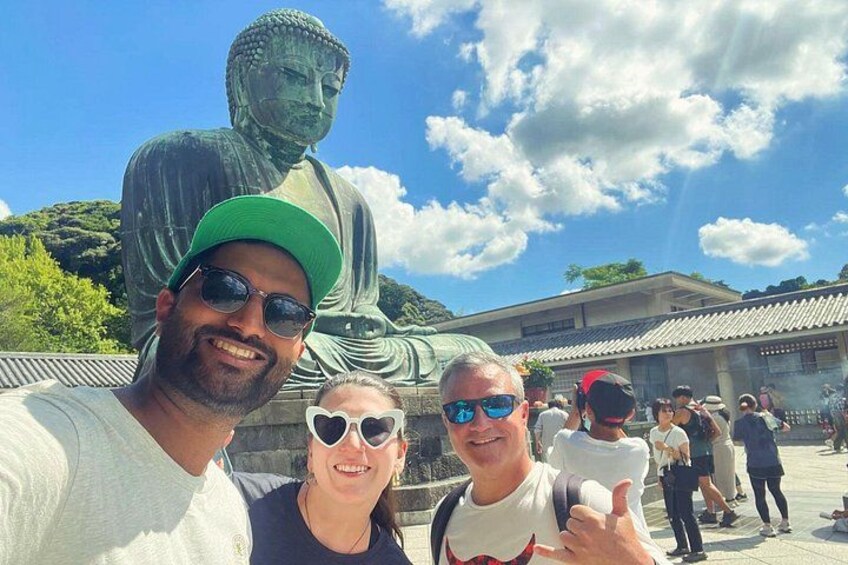 A large Buddha statue, people taking a selfie, and traditional architecture in the background. 4