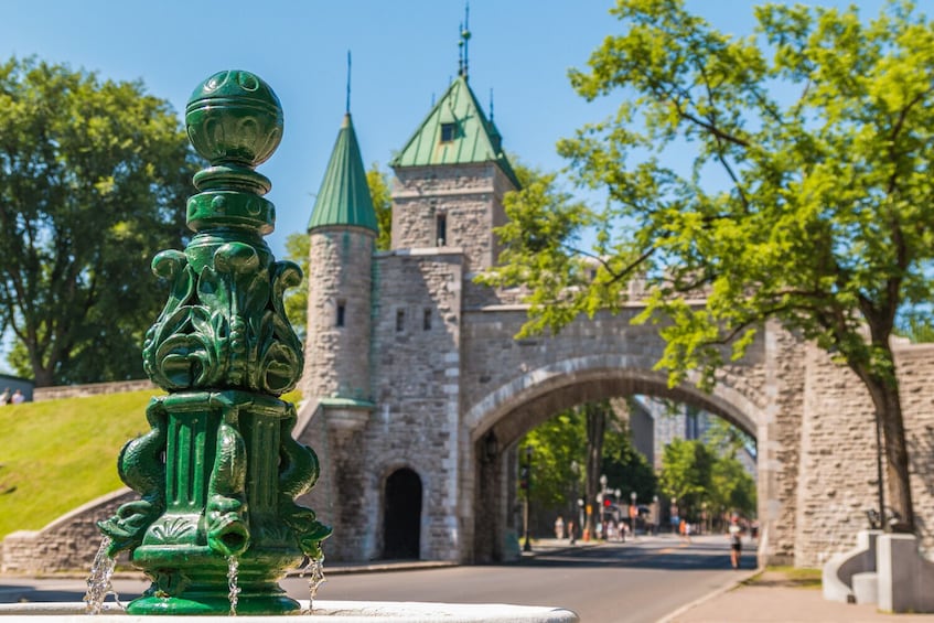 A green ornate fountain in the foreground with a historic stone building and green domes in the background. 5