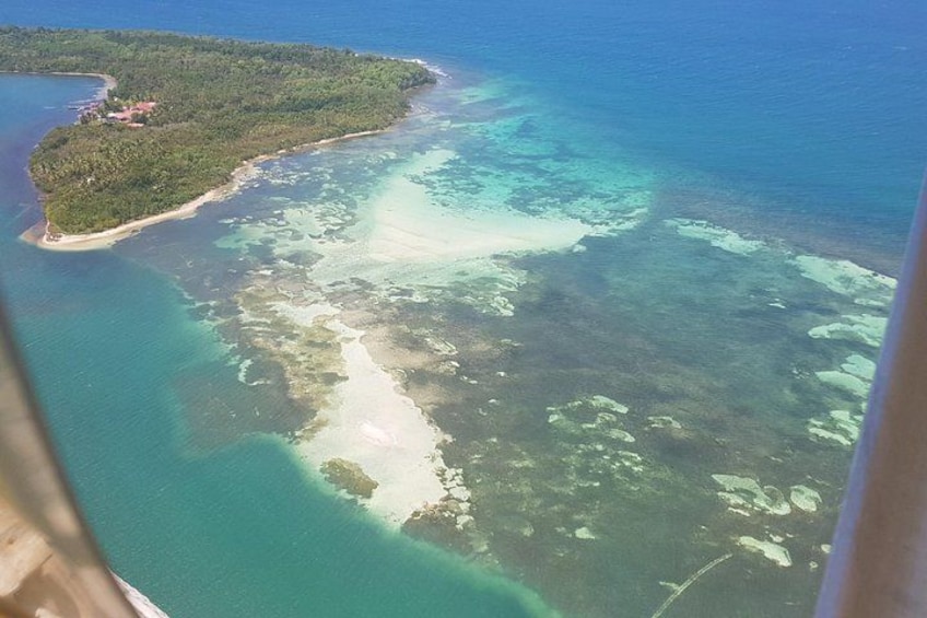 An aerial view of a coastal area with clear turquoise waters, a sandy beach, and a small island with dense vegetation. 4