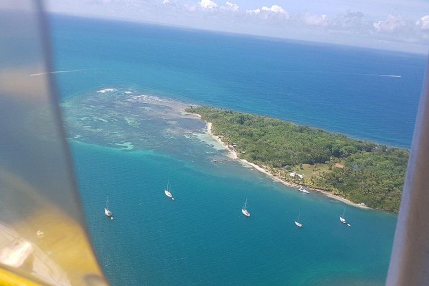 A coastal landscape with clear blue waters, a small island with dense vegetation, and several sailboats anchored near the shore. 3