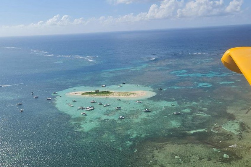 An aerial view of a turquoise lagoon with clear waters, surrounded by a coral reef, and a small island with boats anchored near the shore. 2