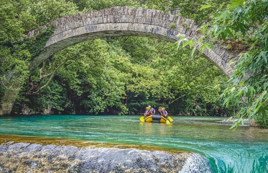 A river with a stone bridge and a group of people in a raft. 1