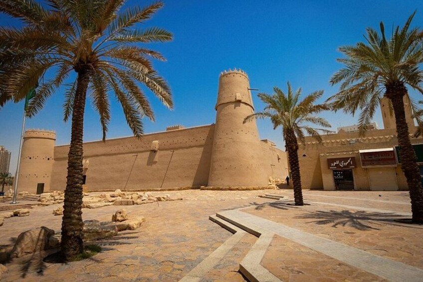Un bâtiment historique doté d’une grande tour, de palmiers et d’une cour dallée. 4