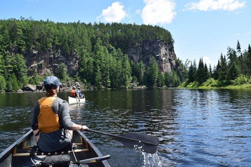 Une personne dans un canoë sur une rivière paisible, entourée d’une forêt dense et de falaises rocheuses. 1