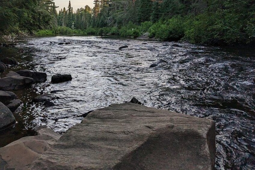 Une rivière qui traverse une zone boisée, avec des rochers dans l'eau et un gros rocher au premier plan. 5