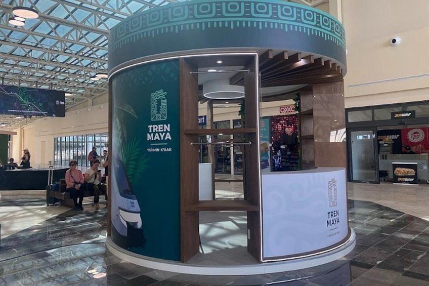 En informations- och försäljningsplats för Tren Maya i ett köpcentrum, med en glasvägg och en digital skärm. 4