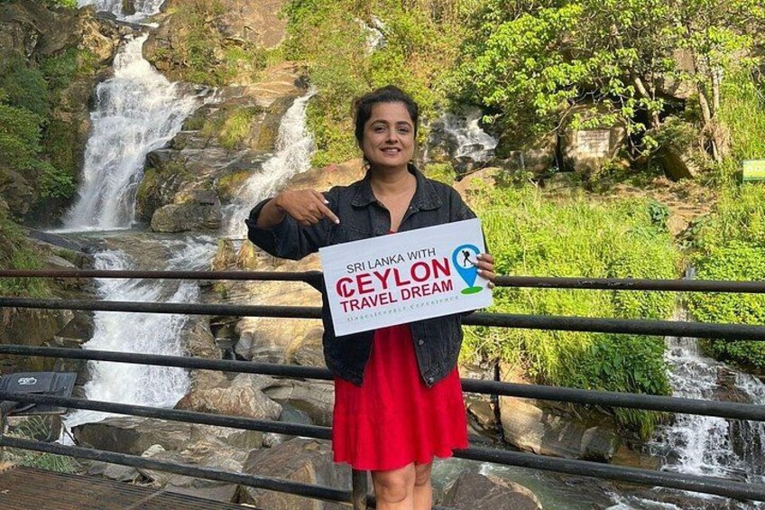 A person standing in front of a waterfall with a sign that reads 'Sri Lanka with Ceylon Travel Dream.' 4