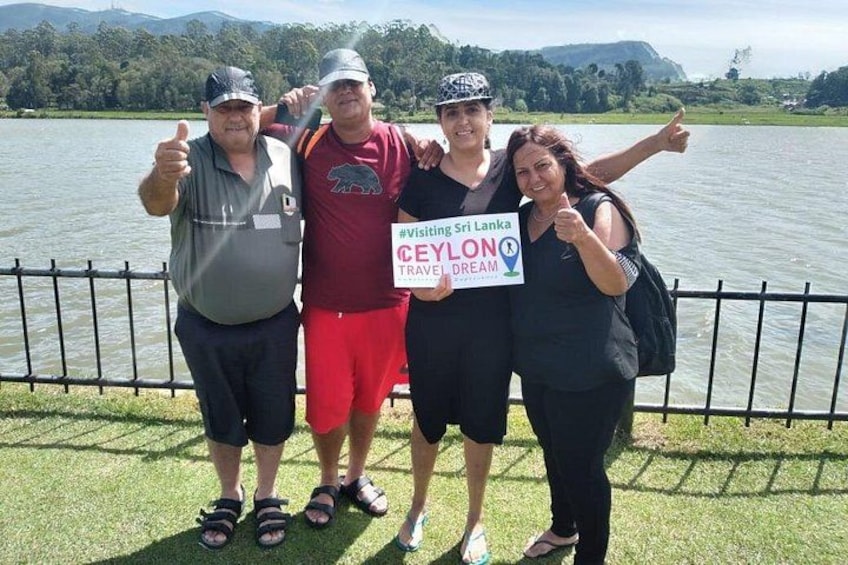 Four people standing by a lake with a sign that reads 'Visiting Sri Lanka Ceylon Travel Dream.' 1