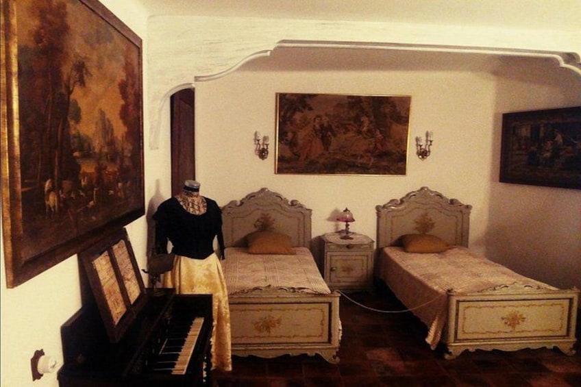 A room with two beds, a piano, and paintings on the walls. 2