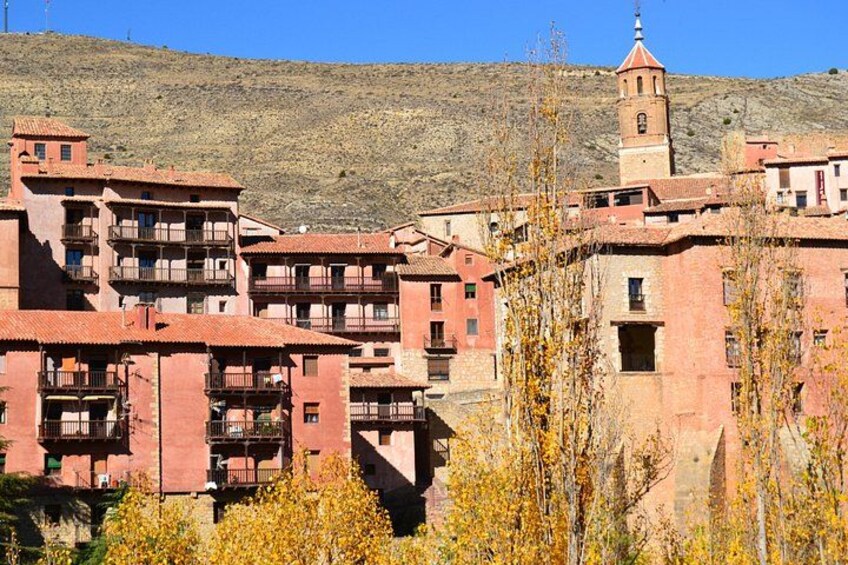 A town with red-roofed buildings, a prominent tower, and a hilly backdrop. 4
