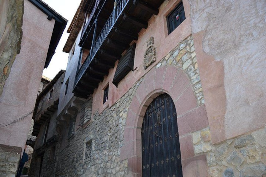 A narrow street with old buildings, a stone wall, and a black arched door. 3