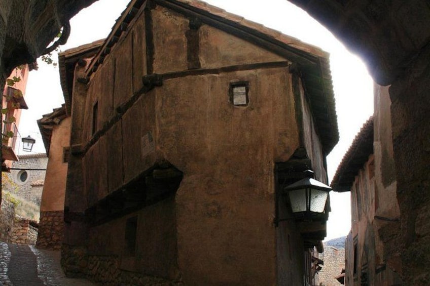 A narrow street with old buildings, a stone wall, and a lantern. 5
