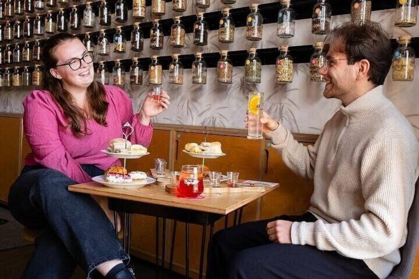 Dos personas sentadas a una mesa con comida y bebidas, con frascos en la pared de fondo. 1