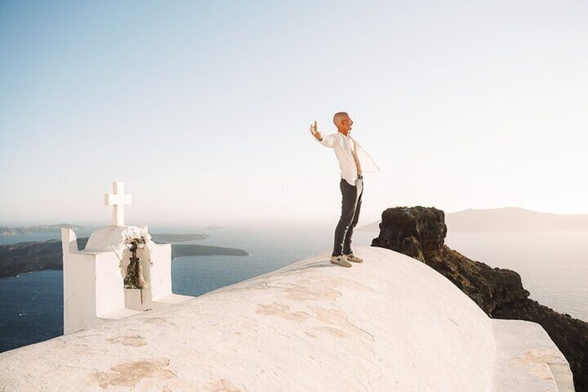 A person standing on a white building with a cross, overlooking a body of water and distant land. 3