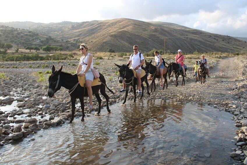 People riding donkeys across a rocky stream with hills in the background. 2