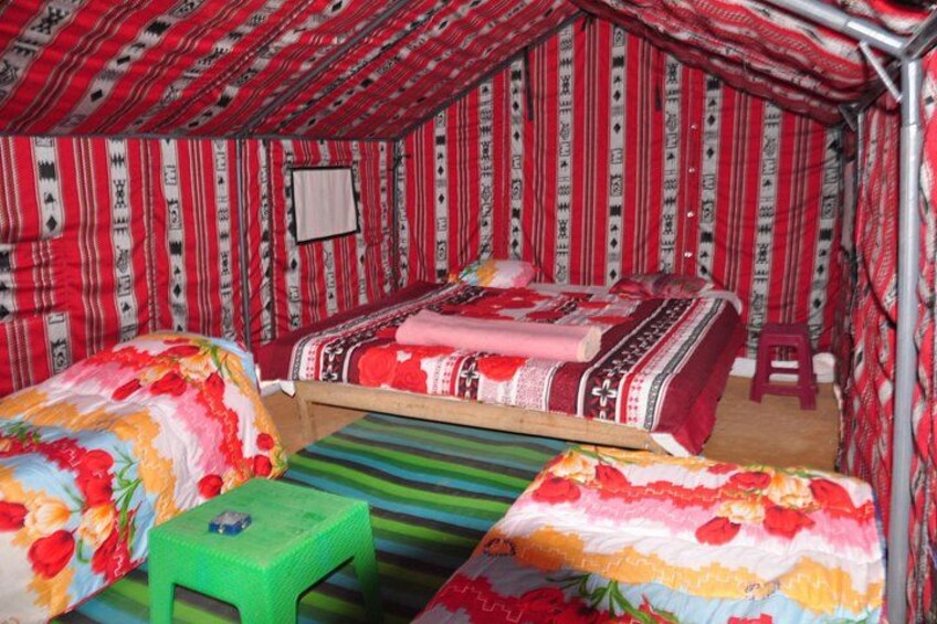 A tent with red and white patterned walls, two beds with floral bedding, and a green stool. 2