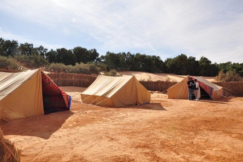 Three beige tents in a desert landscape with sparse vegetation and a clear sky. 5