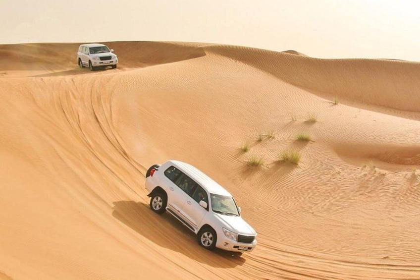 A white SUV navigating a sandy dune in a desert landscape. 1