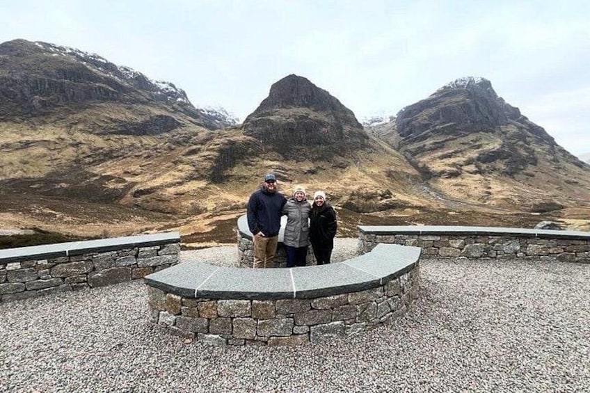 A group of people standing on a circular stone platform with a mountainous landscape in the background. 2