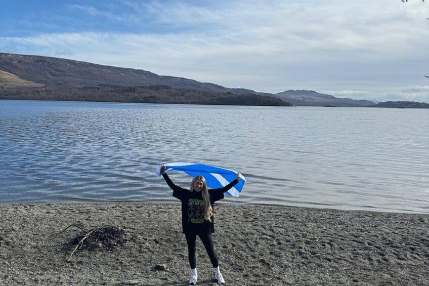 A person holding a blue and white surfboard on a beach with a lake and mountains in the background. 5