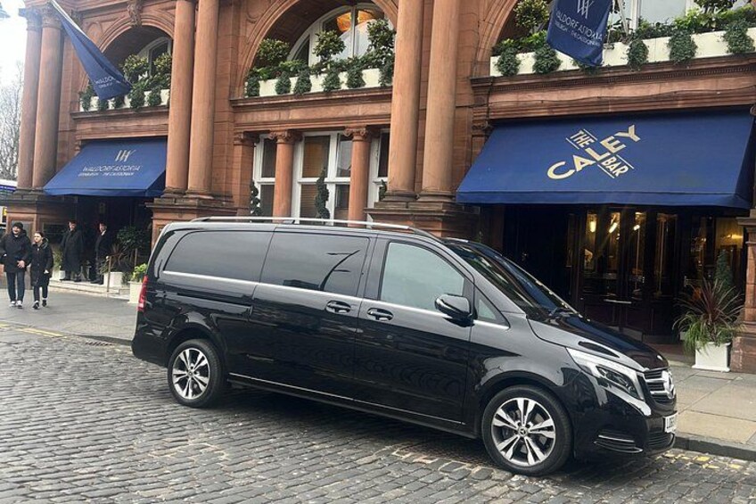 A black minivan parked in front of a building with a blue awning that reads 'THE BAR'. 3