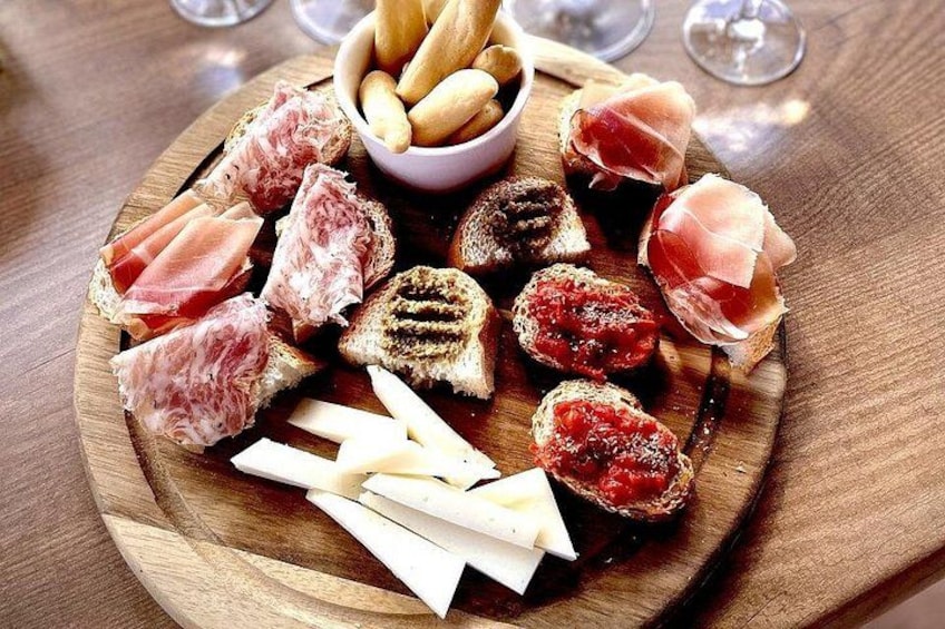 A wooden board with various cheeses, cured meats, and breadsticks. 3