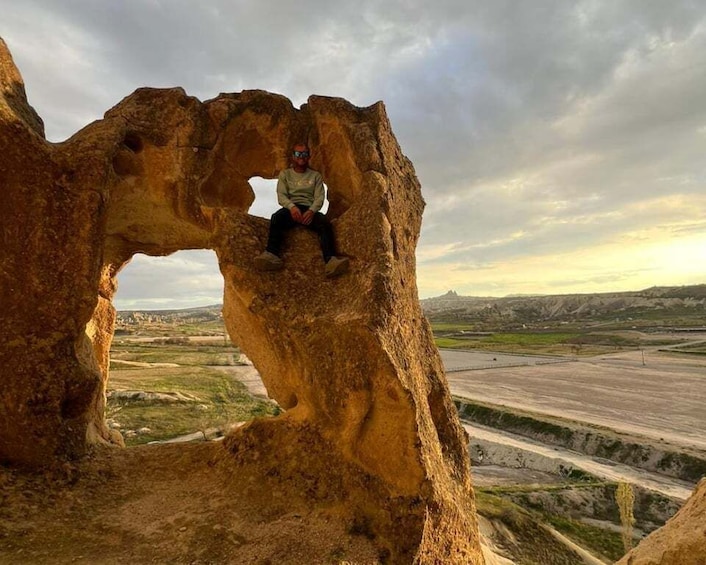 A person sitting on a rock formation with a landscape in the background. 5