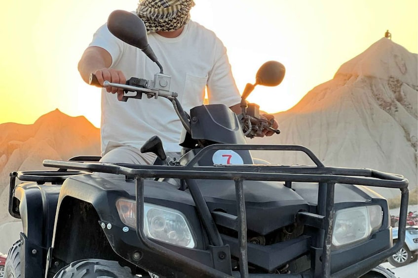 A person riding a black ATV with a number plate '7' in a mountainous area during sunset. 3