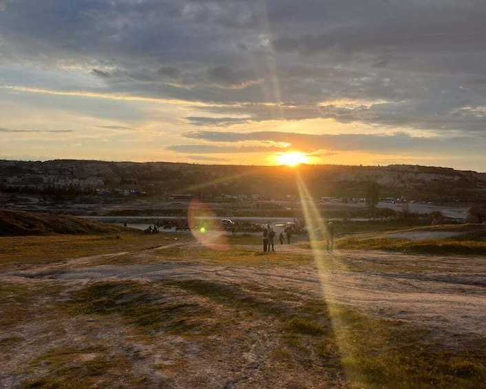 A sunset over a hilly landscape with a group of people standing on a hill. 4