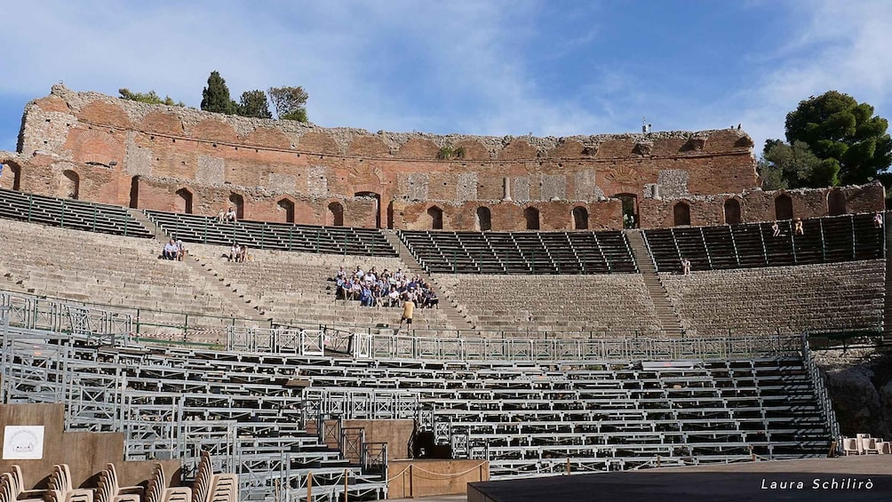 An ancient amphitheater with stone seating and a partially intact stage area. 4