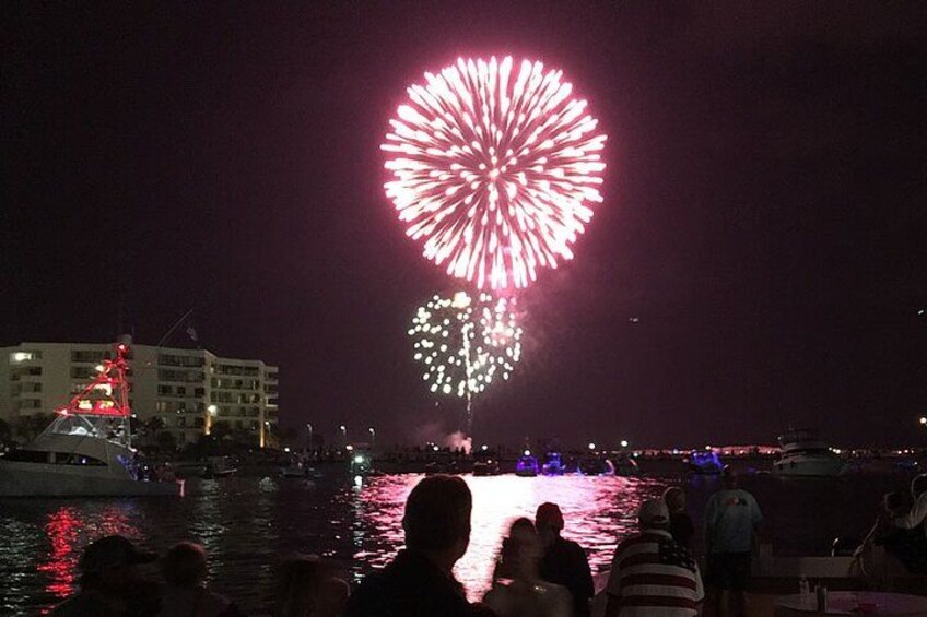 Espectáculo de fuegos artificiales nocturnos sobre un cuerpo de agua, con barcos y edificios al fondo. 2