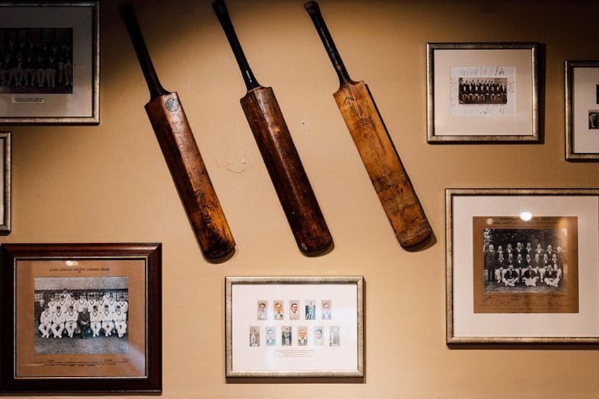 A wall with framed photographs and cricket bats. 2
