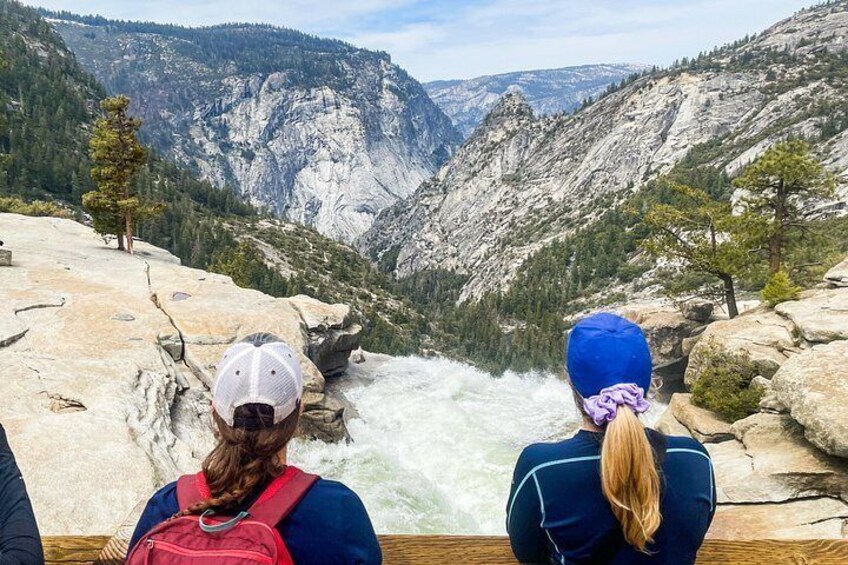 Two people observing a river canyon with steep cliffs and sparse vegetation. 5
